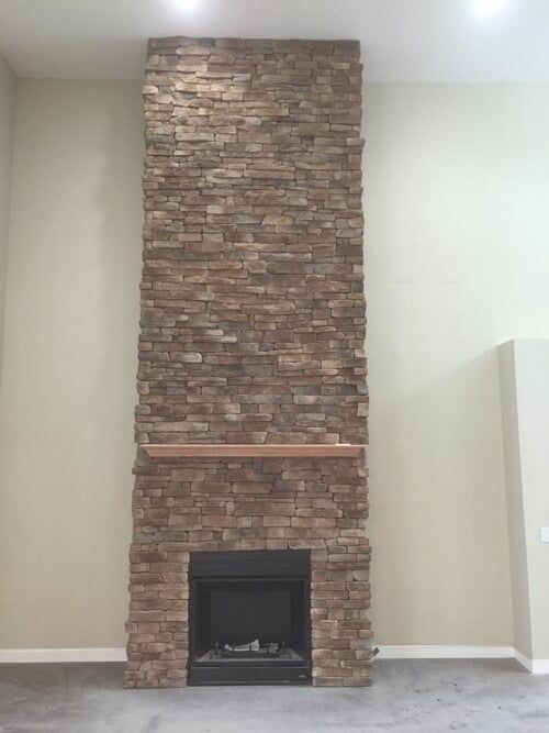 A large stone fireplace with a mantle in an empty room.