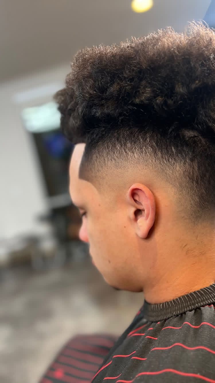 Man with a faded haircut, dark curly hair on top. Profile view.