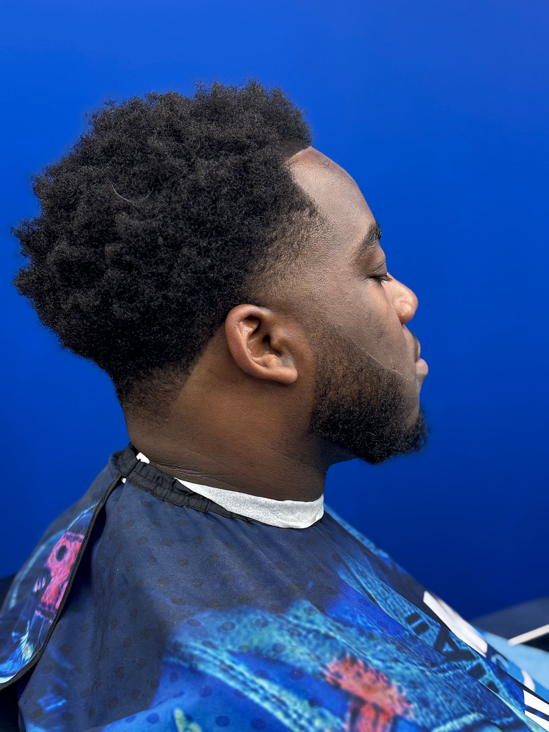 Man with a faded haircut, dark beard, and blue background.