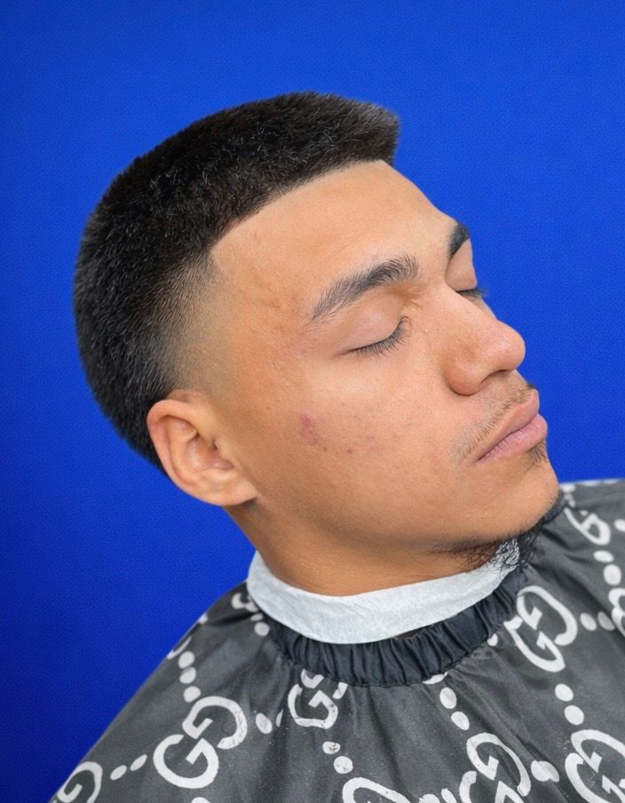 Man with a faded haircut, eyes closed, against a blue background. He wears a cape with a Gucci pattern.