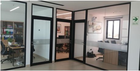 Interior de oficina con paredes de cristal. Se ven escritorios, sillas y un cartel de 