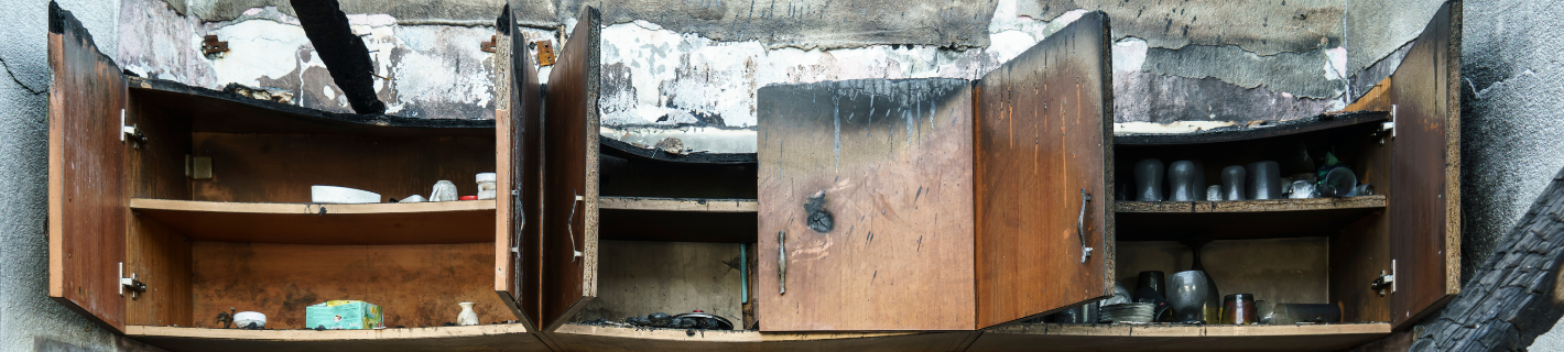 Burnt kitchen cabinets with open doors, showing interior shelves and debris.