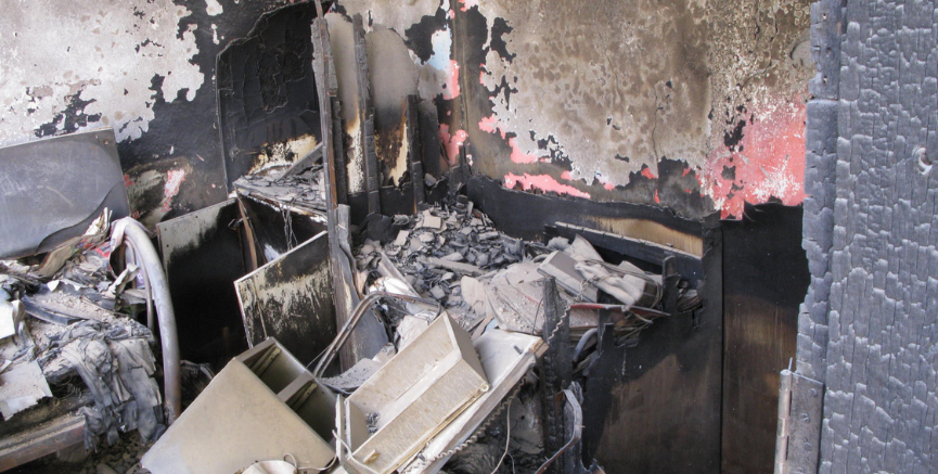 Interior room destroyed by fire, with charred walls, debris, and burnt furniture.