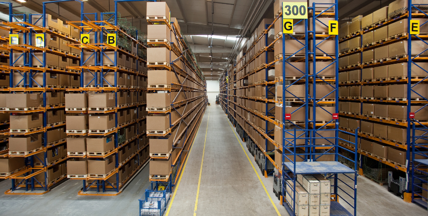 Warehouse interior filled with shelves stacked high with cardboard boxes. Yellow aisle markers.