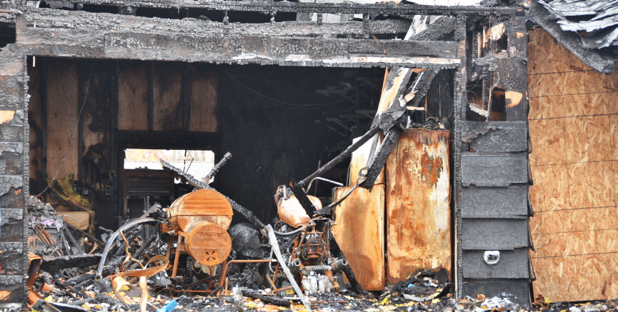 Charred remains of a house after a fire; burnt furniture visible through the open frame.