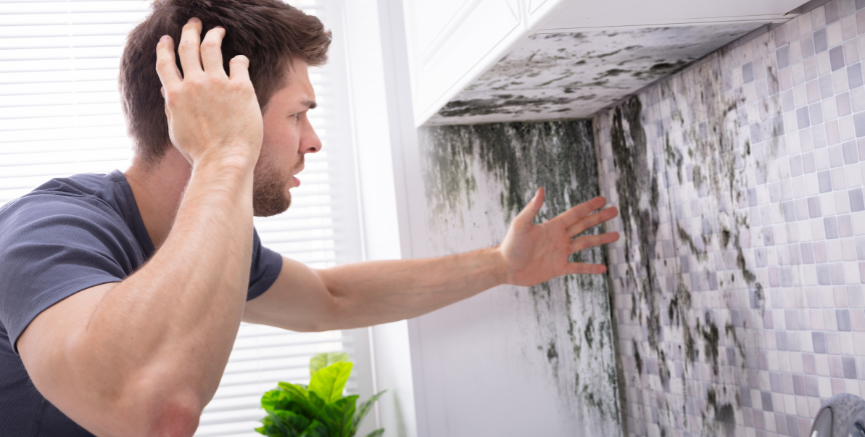 Man reacting with concern to extensive mold growth on bathroom wall.