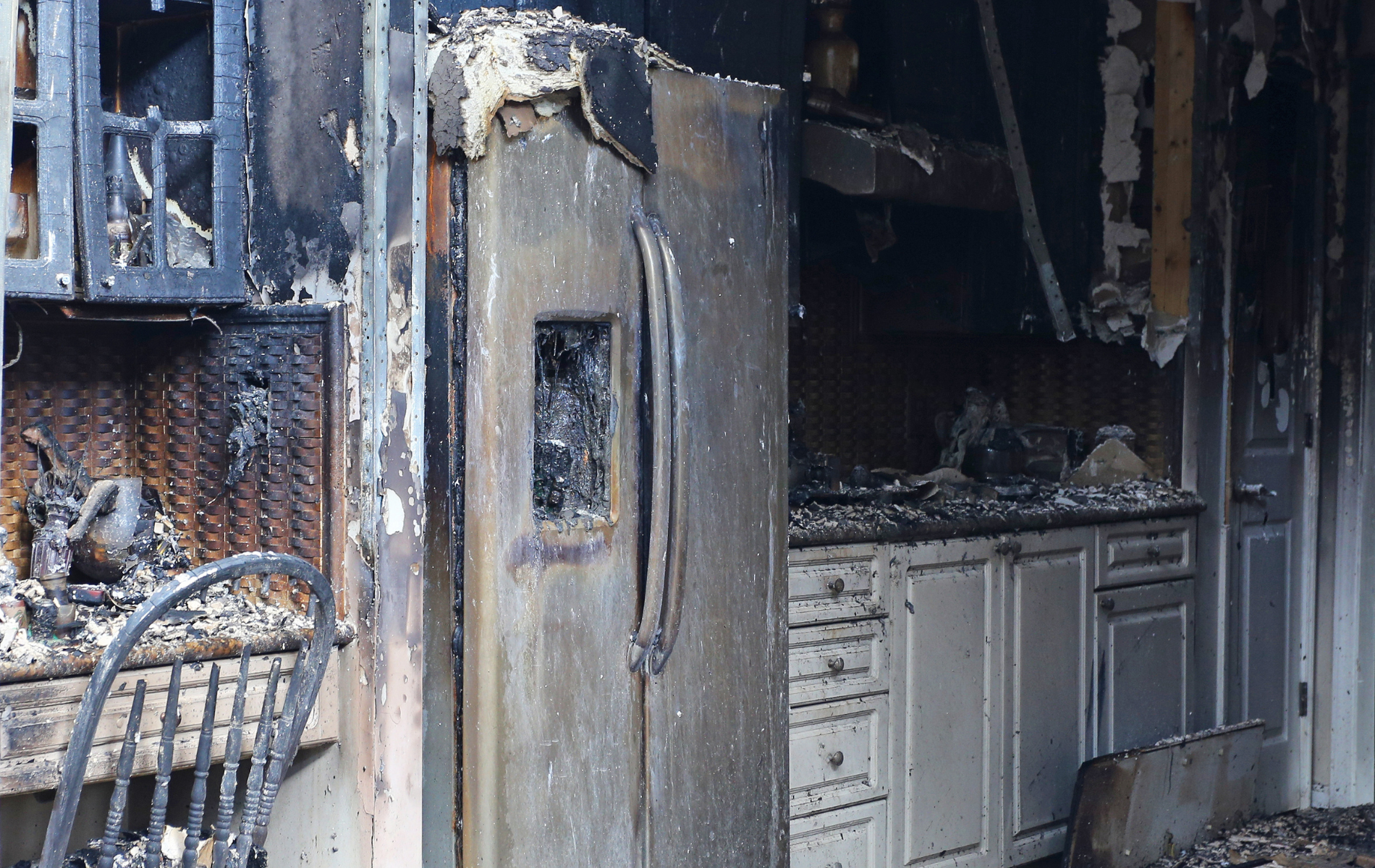 Kitchen interior destroyed by fire; charred refrigerator, cabinets, walls, and window.