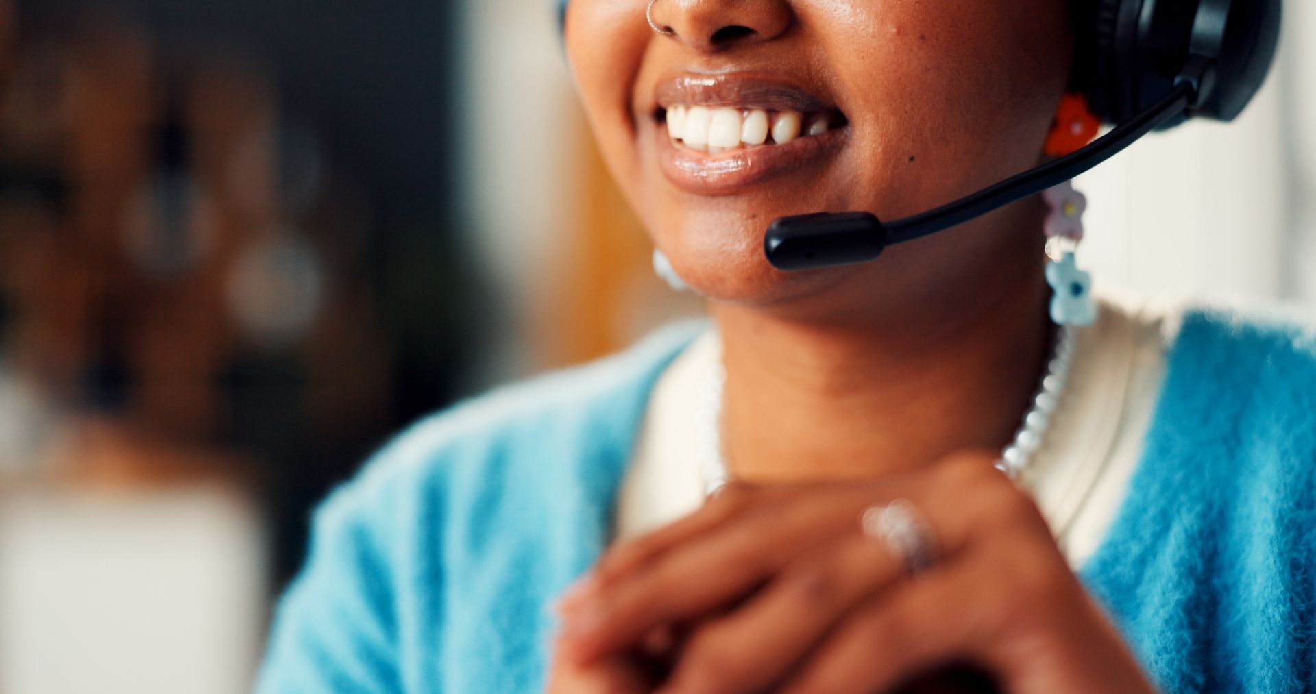 Person wearing a headset smiling, speaking into a microphone. They are wearing a blue sweater and earrings.