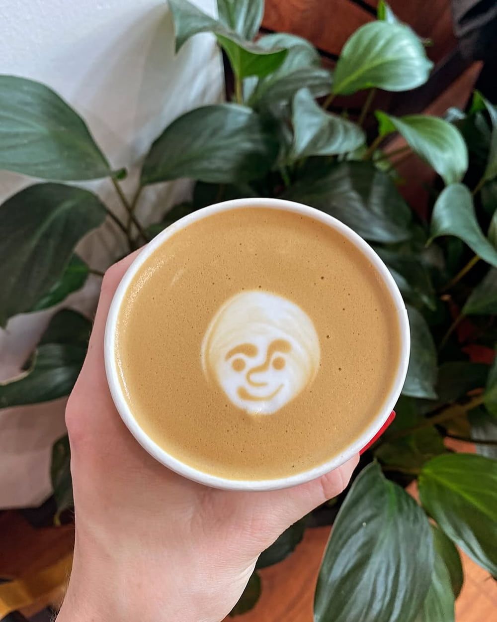 A Person is Holding a Cup of Coffee With a Face Drawn on It — Swish Cafe in Ballina, NSW