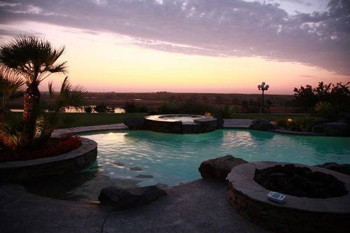 A large swimming pool with a fire pit in the middle at sunset.