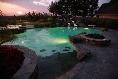 A large swimming pool is lit up at night in a backyard.