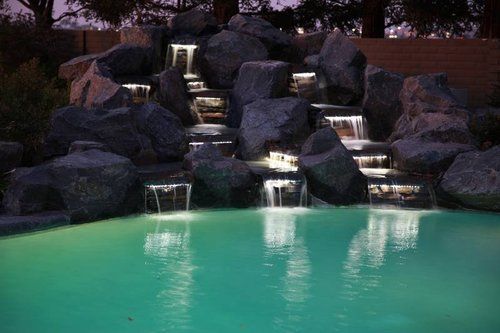 A waterfall in the middle of a swimming pool at night.
