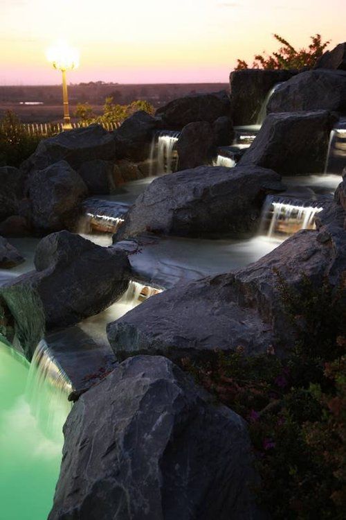 A swimming pool surrounded by rocks and a waterfall at sunset
