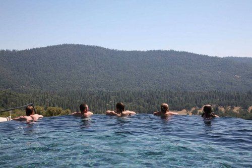 A group of people are swimming in an infinity pool with mountains in the background.