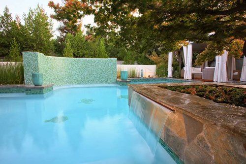 A large swimming pool surrounded by trees and a stone wall.