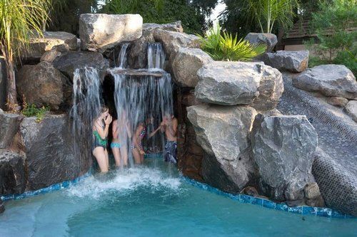 A group of people are standing in front of a waterfall in a pool.