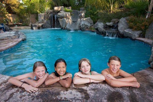 A group of young girls are laying on the edge of a swimming pool.