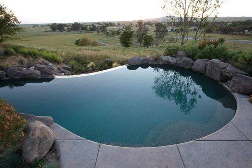 A large swimming pool surrounded by rocks and grass with a view of a field.
