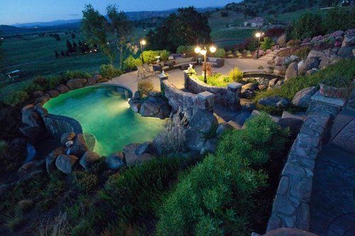 An aerial view of a large swimming pool at night surrounded by trees and rocks.