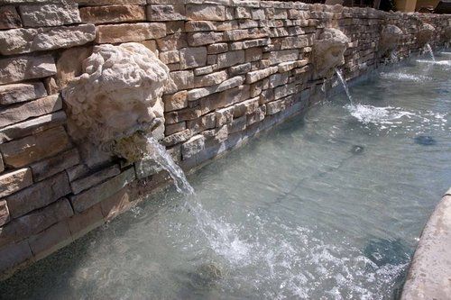 A fountain with a statue of a man 's head is surrounded by a stone wall.