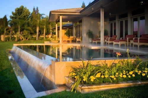 A large swimming pool with a waterfall in front of a house.