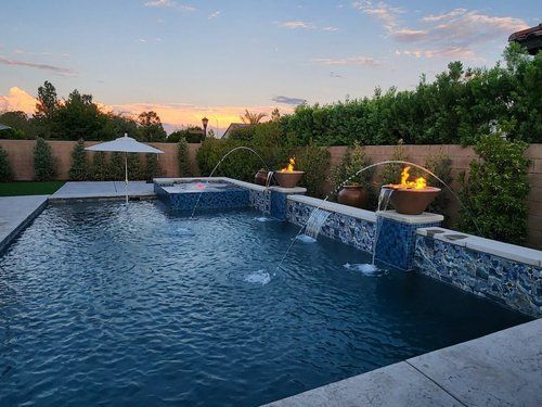 A large swimming pool with a fountain and umbrella in the backyard.