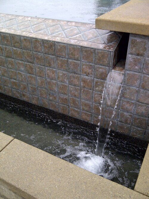 A waterfall is coming out of a tiled wall into a pool.