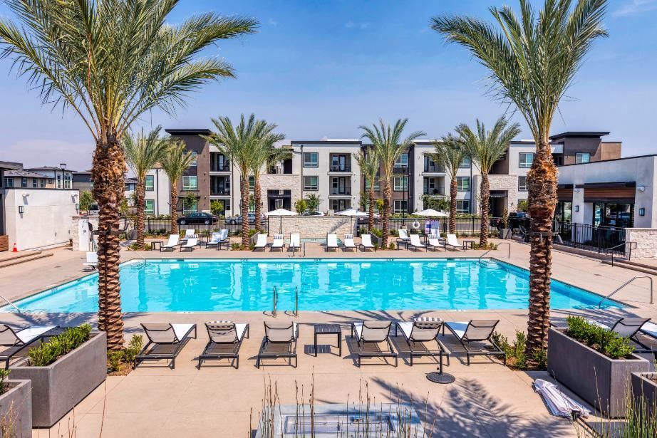 A large swimming pool surrounded by palm trees and chairs in front of a building.