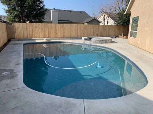 A large swimming pool in the backyard of a house with a wooden fence.