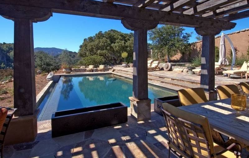 A patio with a table and chairs and a large swimming pool