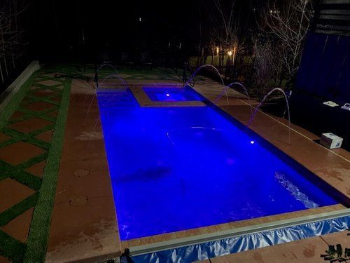 A large swimming pool is lit up at night with blue lights.