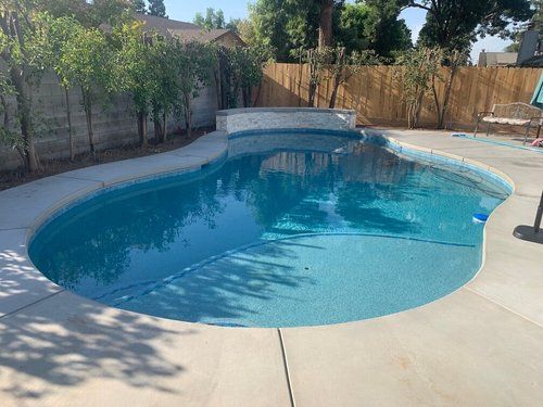 A large swimming pool is surrounded by trees and a fence.
