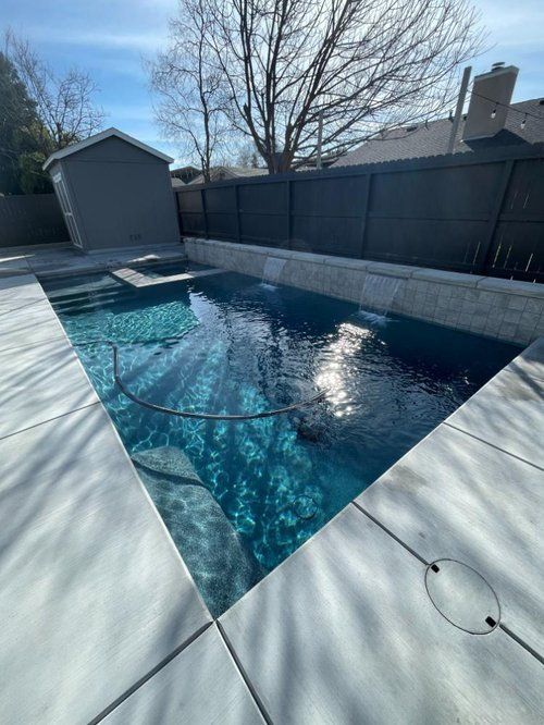 A large swimming pool is surrounded by a fence and a shed.