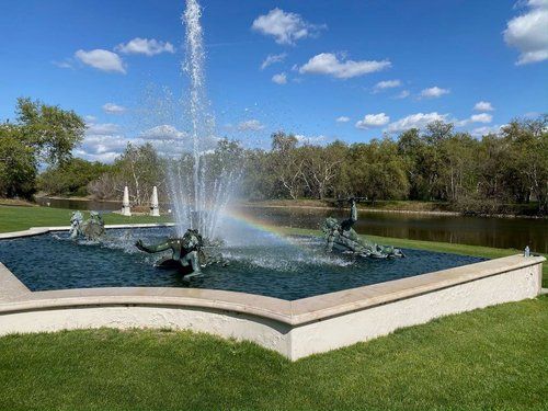 A fountain in a park with a rainbow in the water.