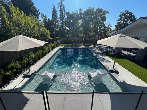 A large swimming pool surrounded by chairs and umbrellas in a backyard.