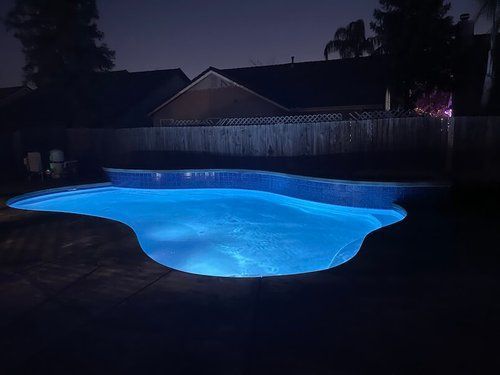 A swimming pool is lit up at night with blue lights.