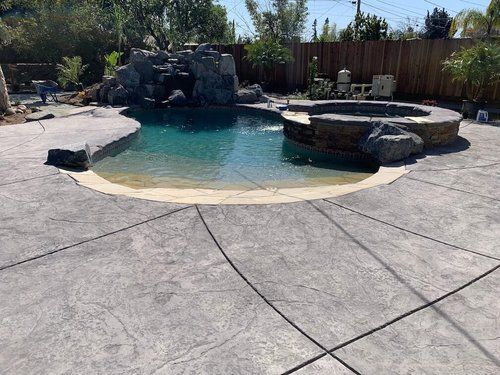 A large swimming pool with a hot tub and a waterfall in the backyard.