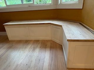 A wooden bench is sitting in a room next to a window.