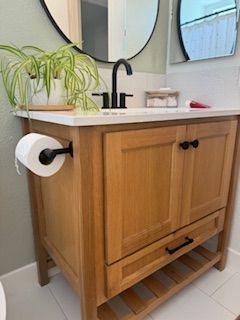 A bathroom with a wooden vanity , sink , mirror and toilet paper holder.