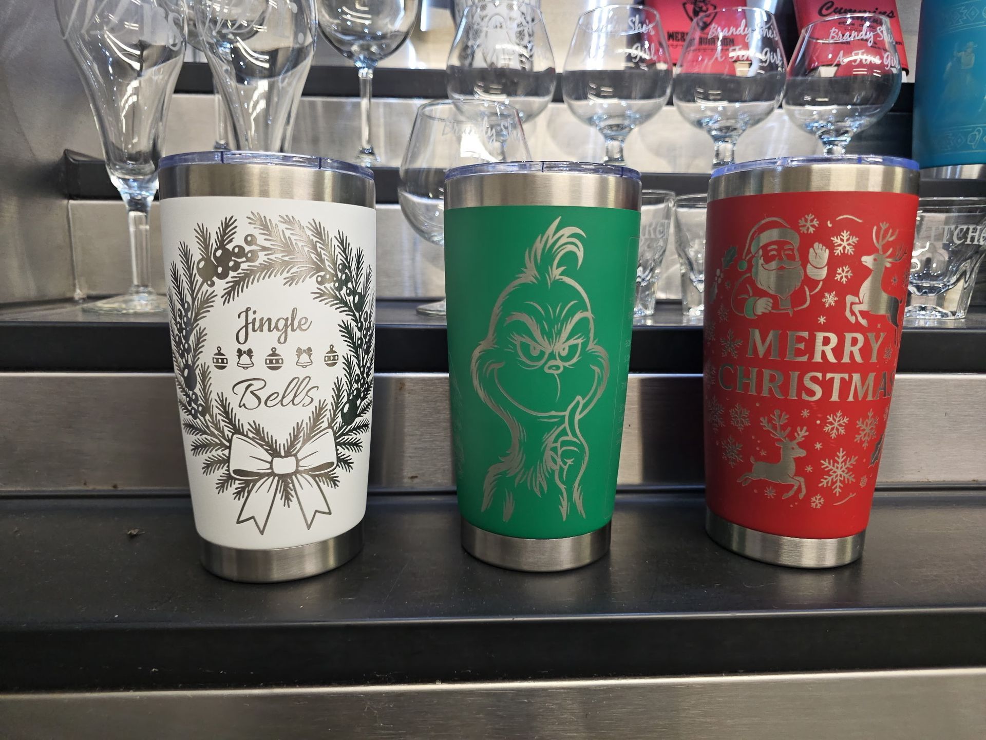 A row of colorful personalized tumblers and water bottles sits on a wooden board, with two smaller cups in the front.