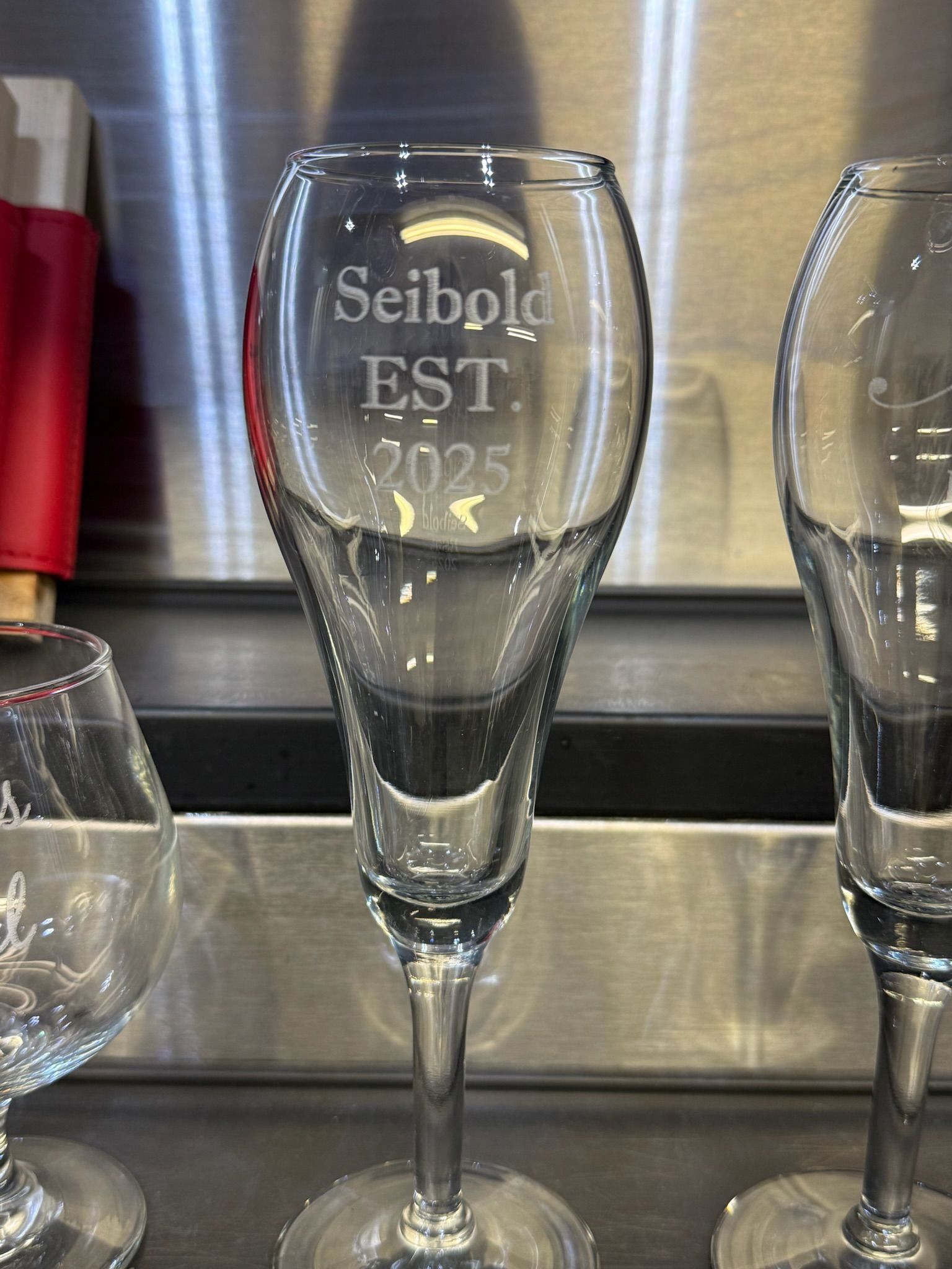 A clear, tall champagne flute stands centered on a white curved surface against a dark background.