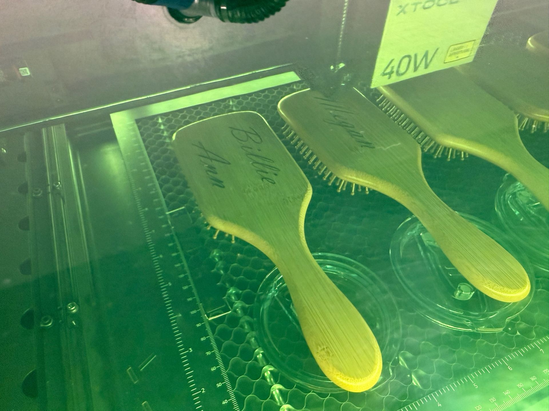 A laser engraver burns an intricate, symmetrical fern-like design into the surface of a light-colored wooden box.