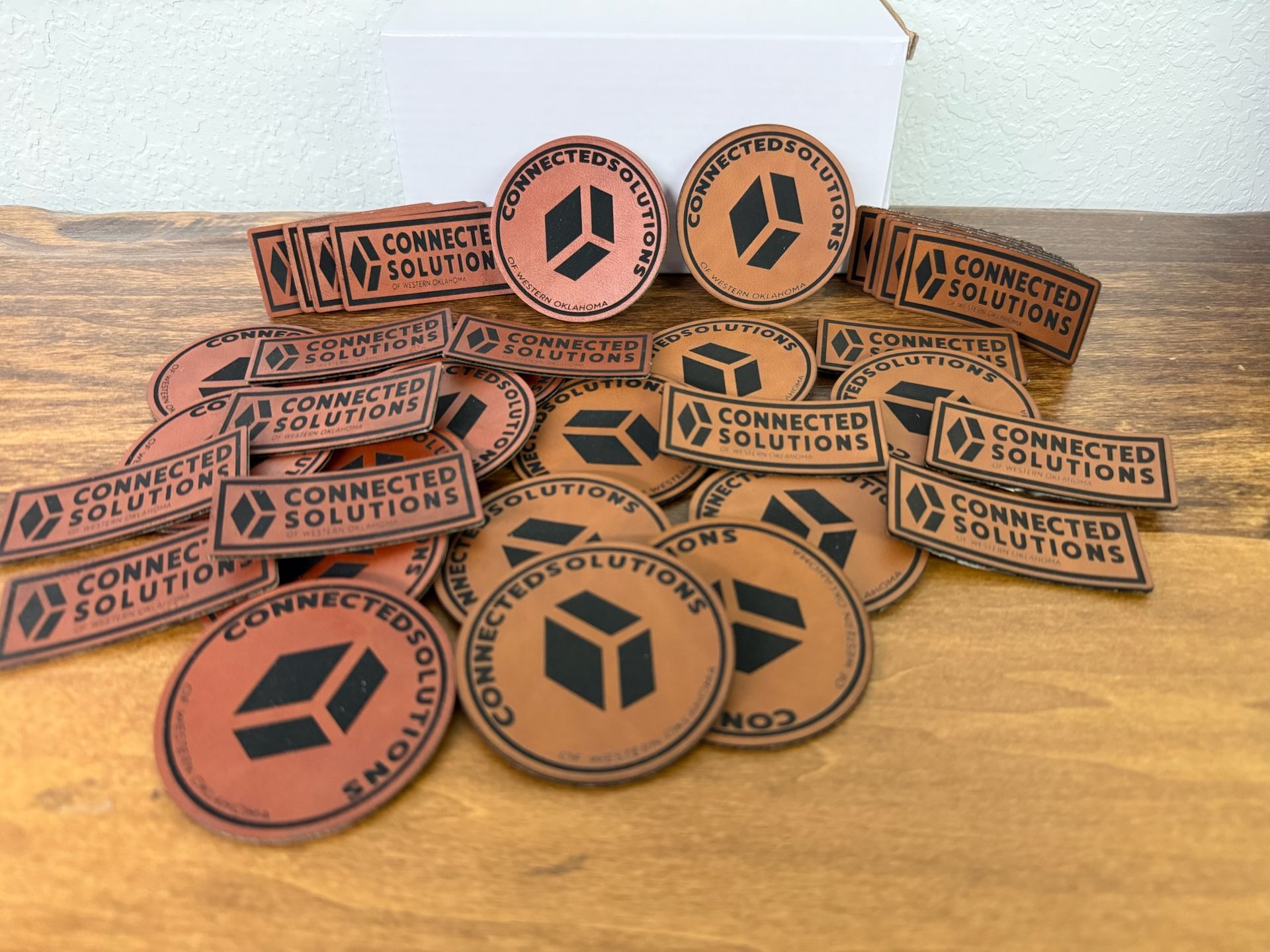 A collection of round and rectangular brown leather patches featuring a cube logo and the text 