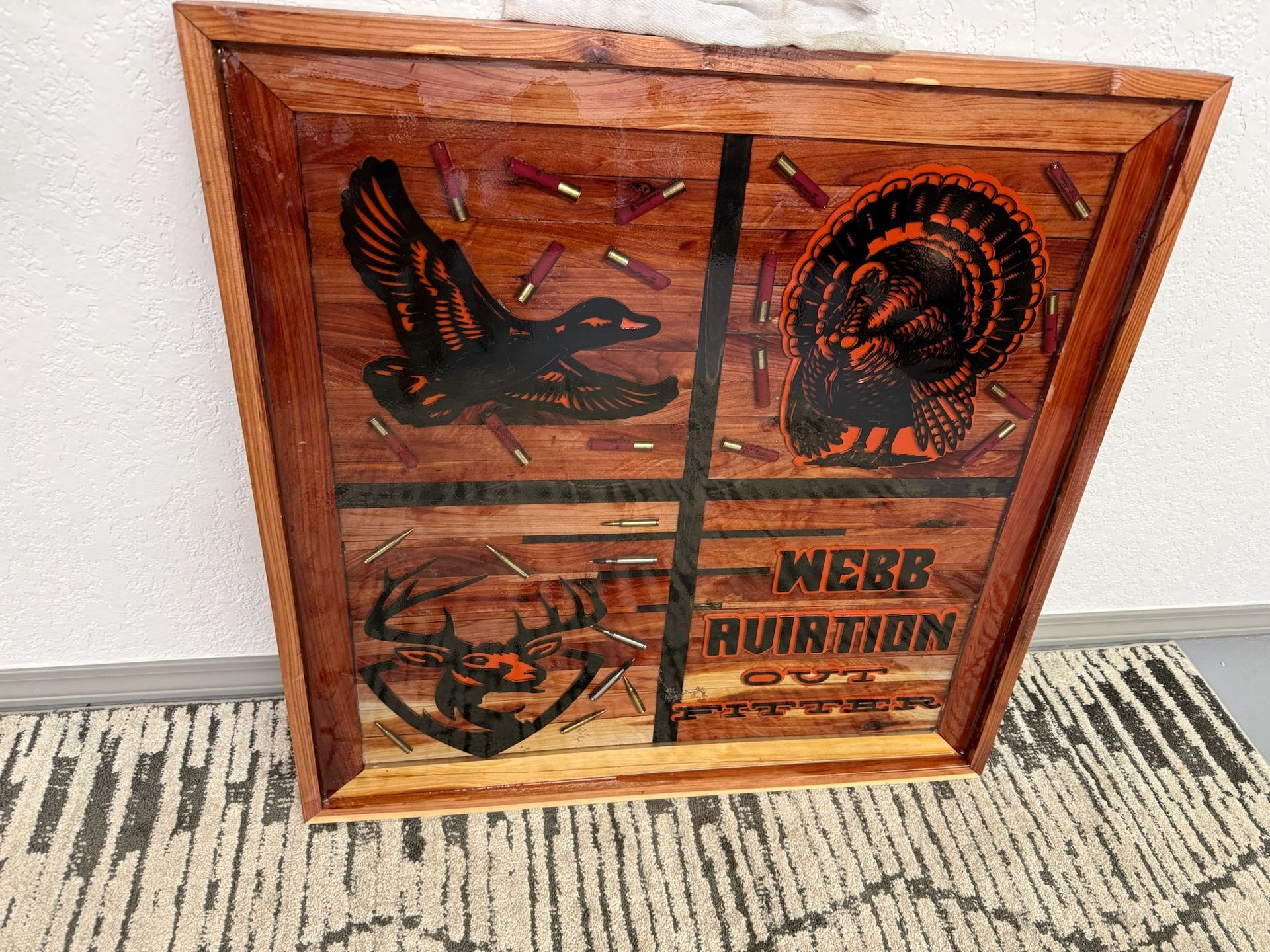 A wooden framed wall art piece featuring silhouettes of a duck, turkey, and deer, decorated with bullet casings.