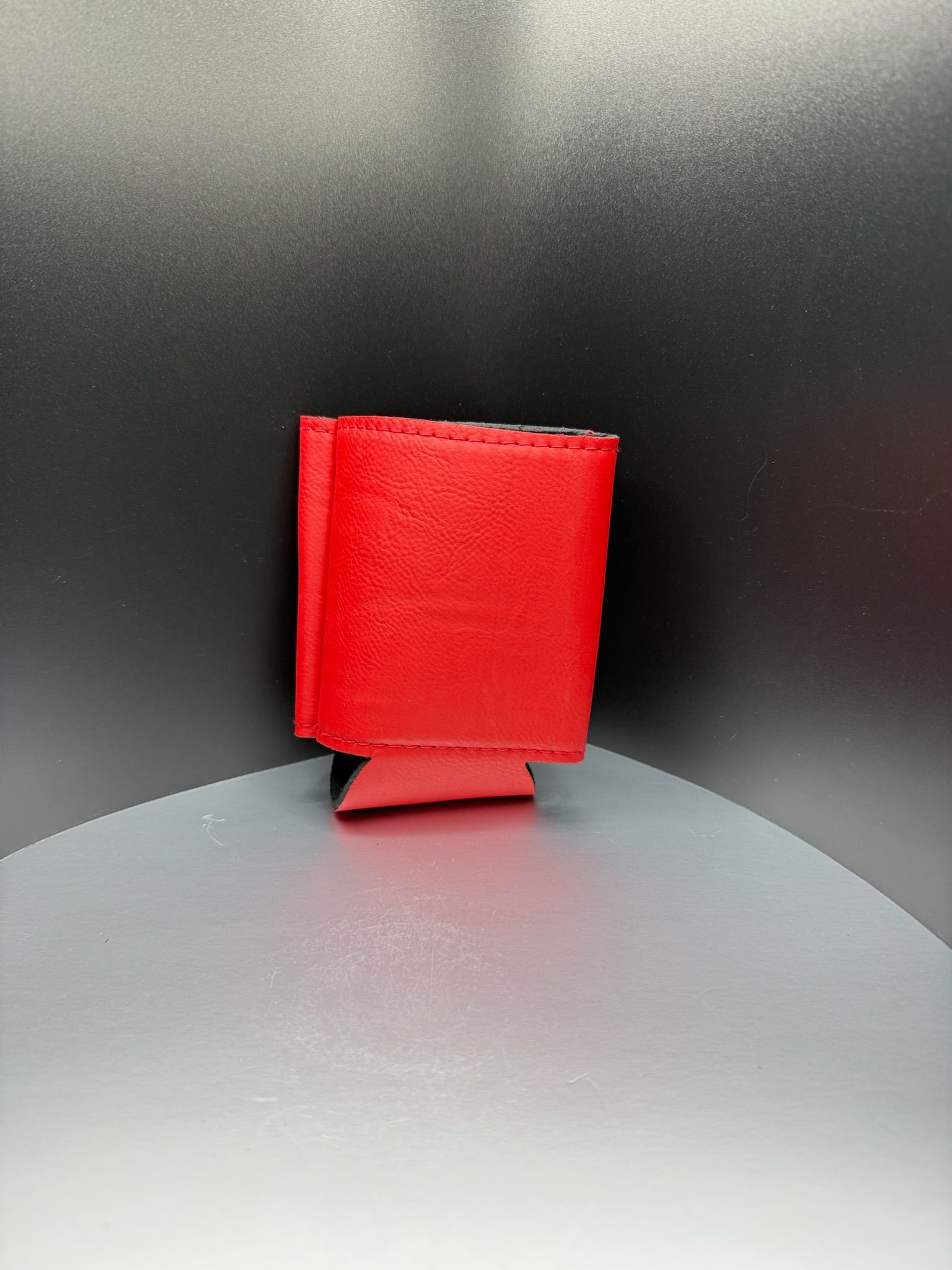 A bright red foam beverage koozie standing upright against a dark, minimalist background.