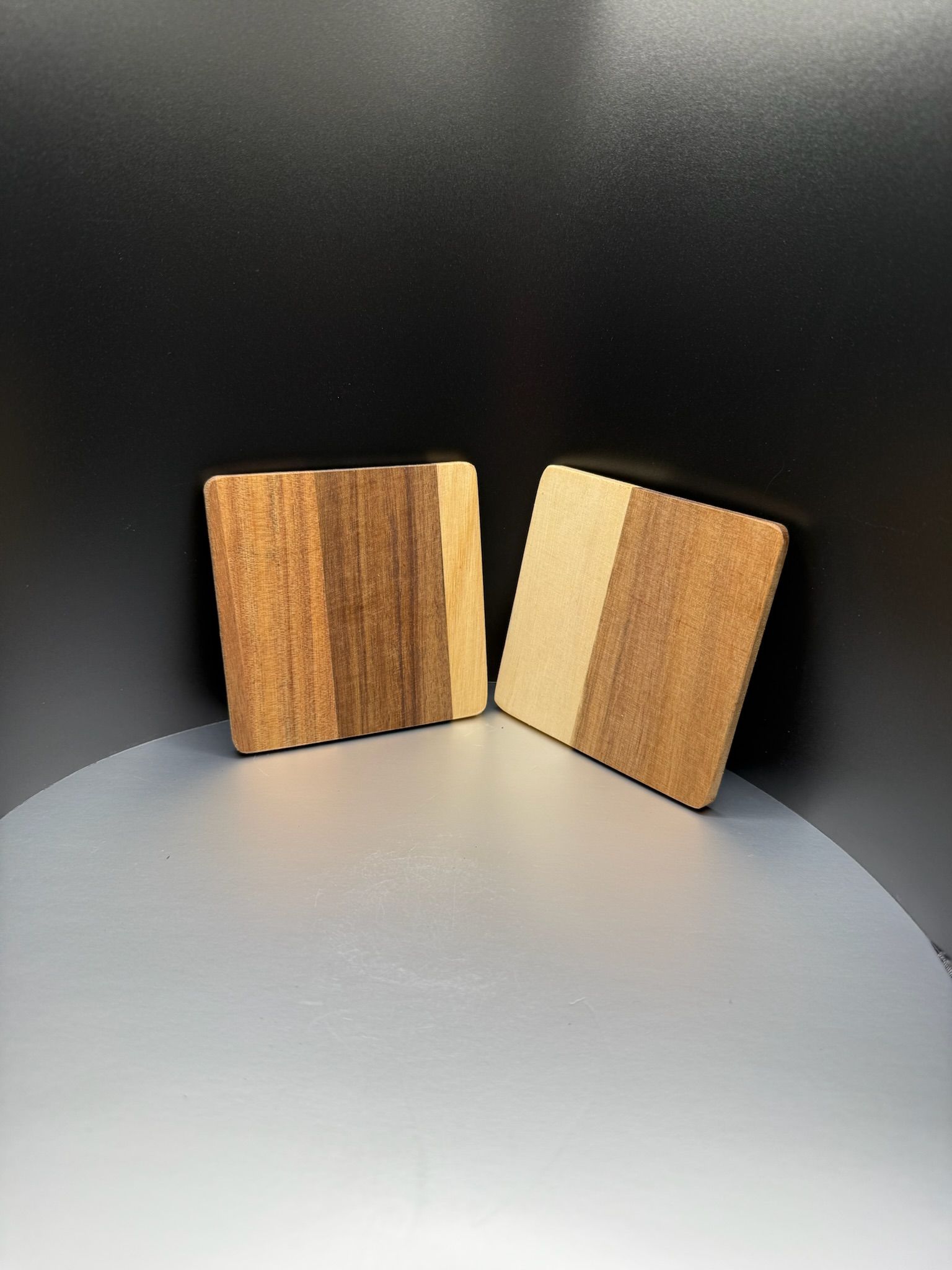 Two square wooden coasters with light and dark brown vertical stripes, set against a dark background.