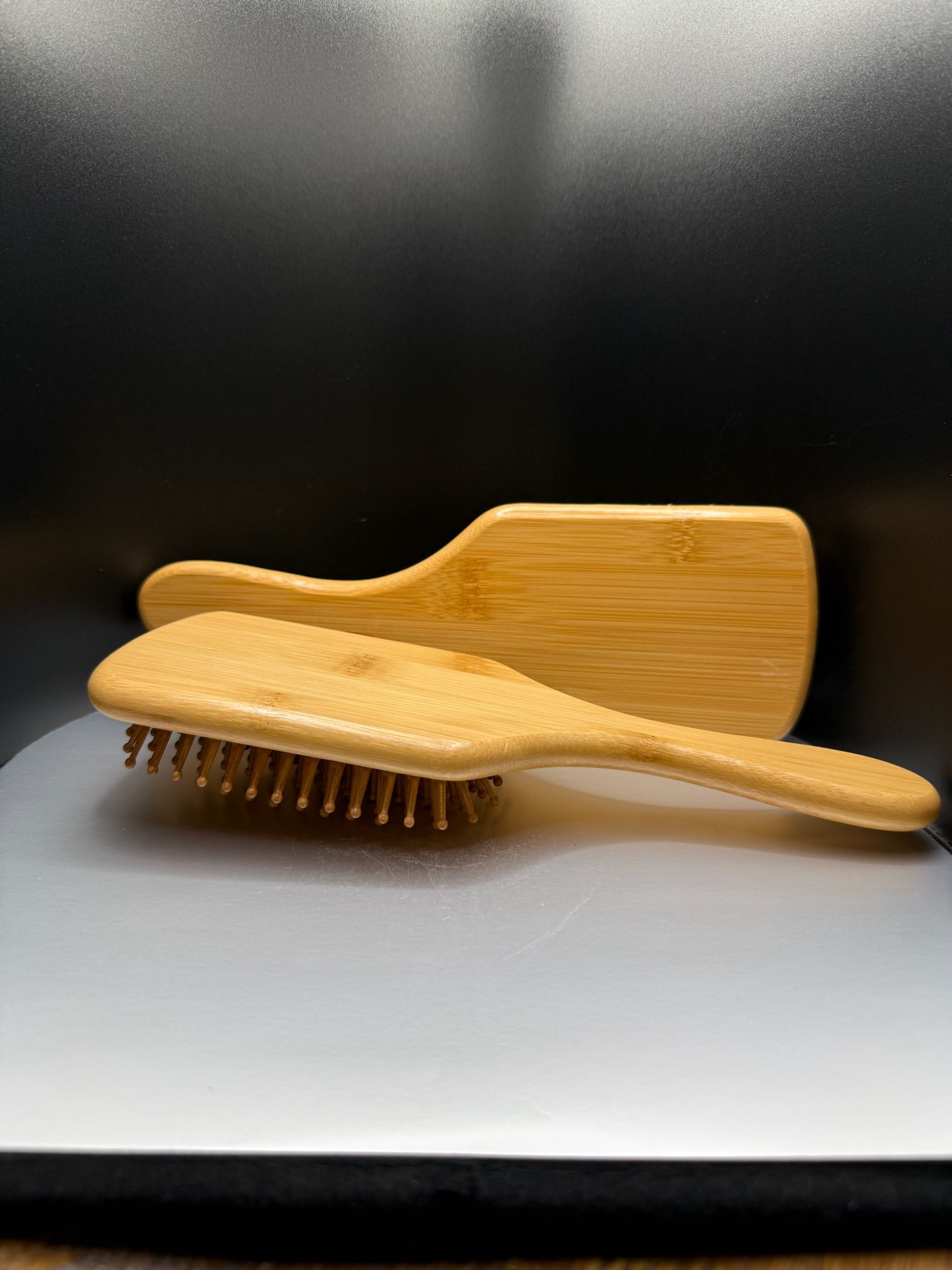 Two wooden hairbrushes stacked on a gray surface against a black background.
