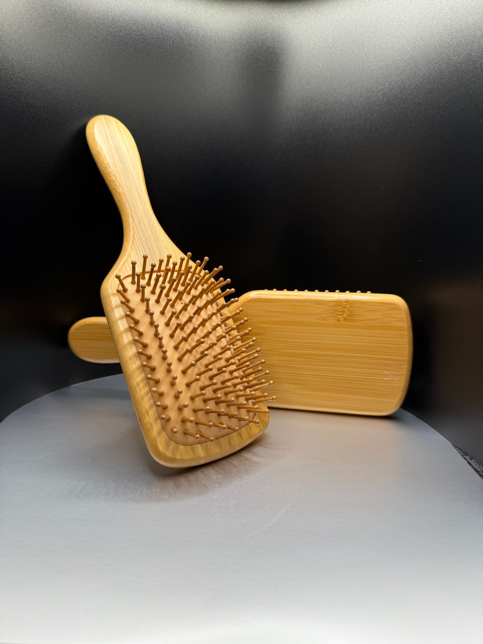 Two wooden hairbrushes stacked on a gray surface against a black background.