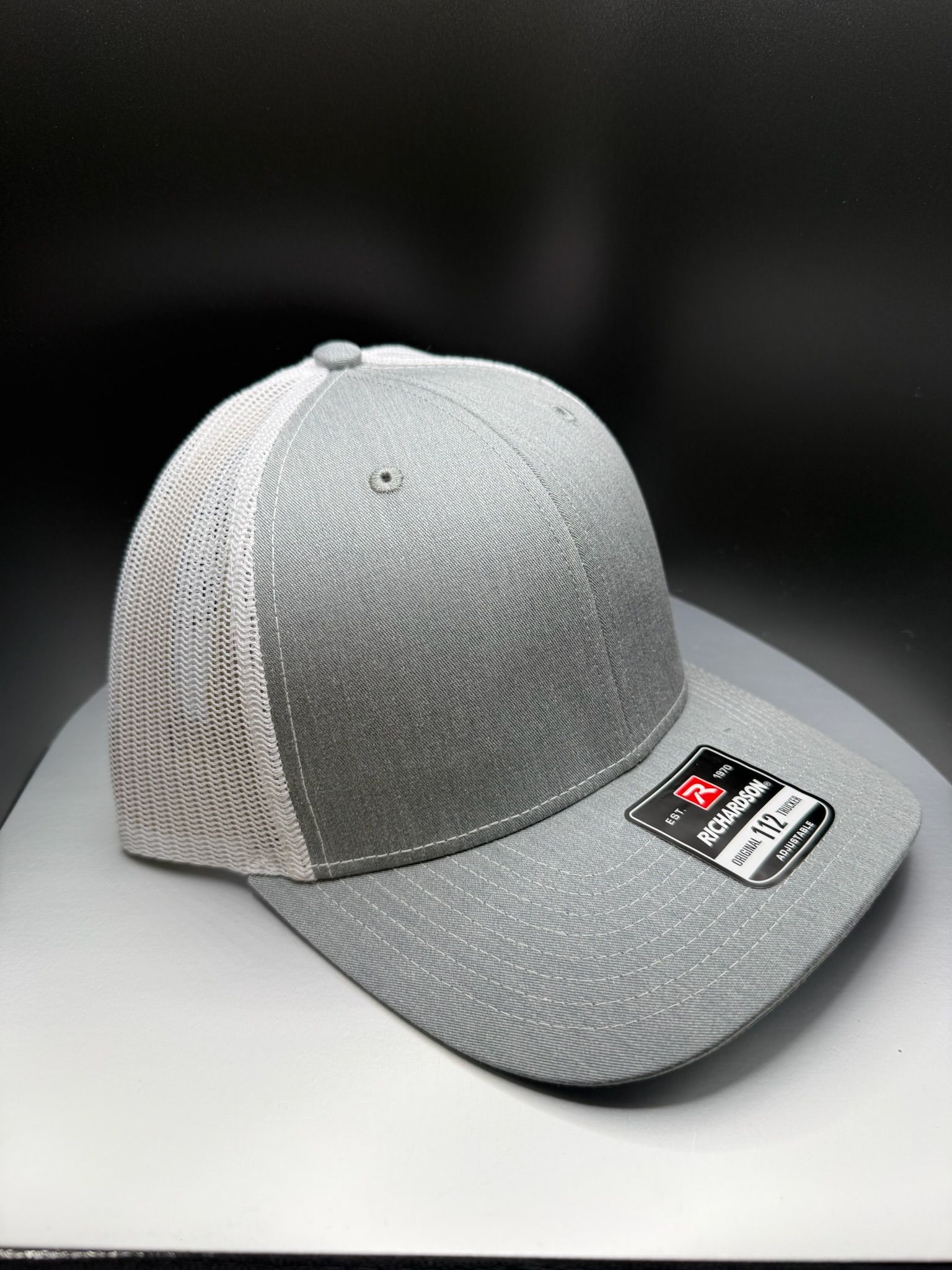 A grey baseball cap with a white mesh back and a sticker on the flat visor, centered on a light grey surface.