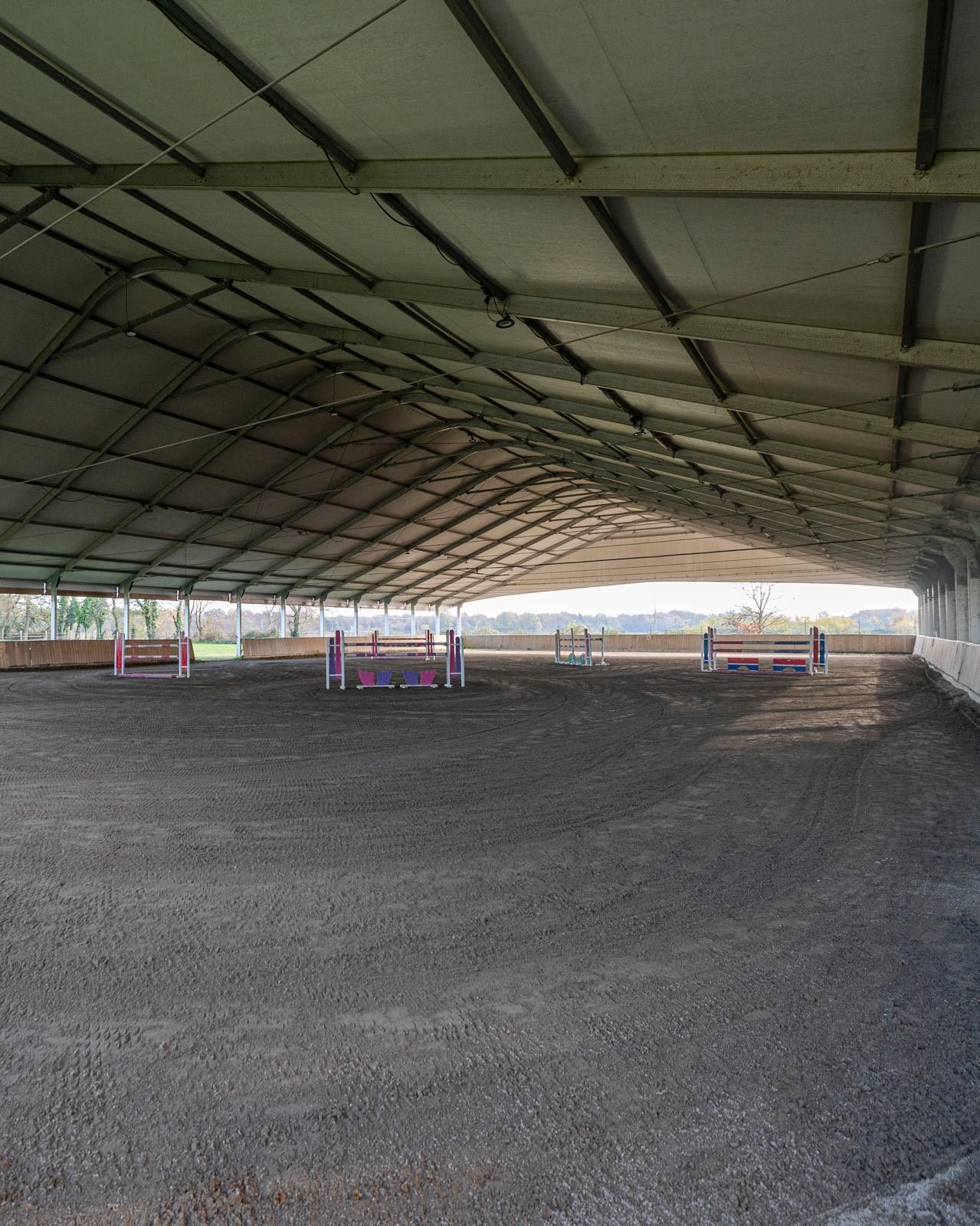 Maneggio coperto con ostacoli, coperto da un grande tetto e illuminato dal sole.
